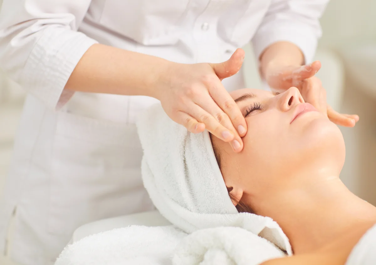 Therapist giving a relaxing facial massage to a client with a towel wrapped around her hair