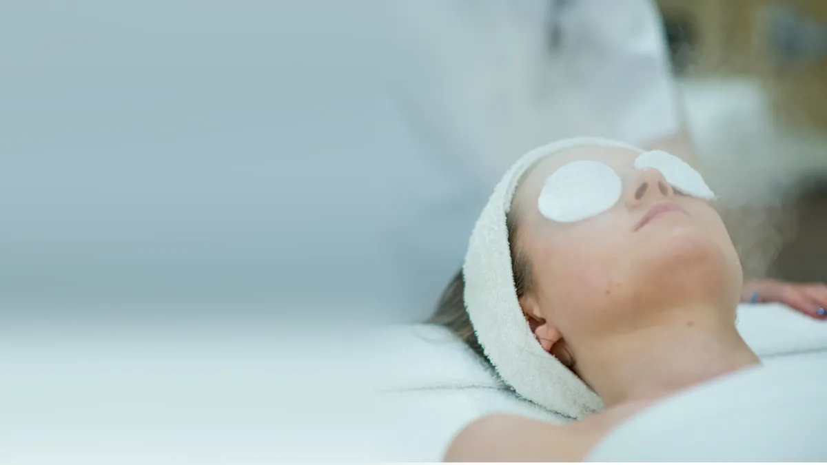 Client relaxing under facial steam with cotton eye pads